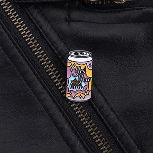 Detail showing 'Yes You Can' enamel soda can pin on a black leather jacket texture
