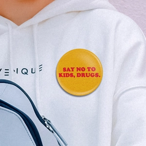 Gros plan d'un badge rond jaune avec slogan rouge épinglé sur un sweat à capuche blanc