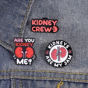 Detailed view of three creative kidney enamel pins pinned on light blue denim fabric