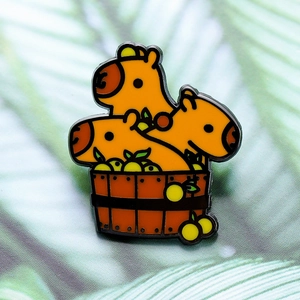 Creative enamel pin featuring three cute capybaras bathing in a wooden barrel with yuzu