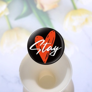 Dettaglio di una spilla in latta nera con cuore rosso e scritta Stay su un vaso ceramico