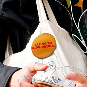 Détail d'un badge rond orange avec slogan rouge fixé sur une bandoulière en toile