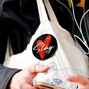 Dettaglio di una spilla rotonda nera con cuore rosso e scritta Stay sulla tracolla di una borsa