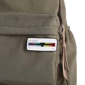 Gros plan du pin's interactif en émail avec curseur d'humeur sur un sac à dos vert