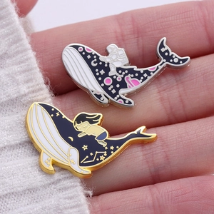 Detail of cute whale enamel pins with galaxy and sea motifs held in hand