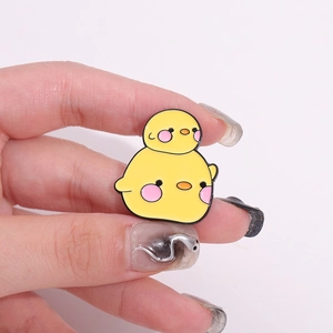 Gros plan d'une jolie broche poussin en émail jaune tenue à la main pour montrer la taille