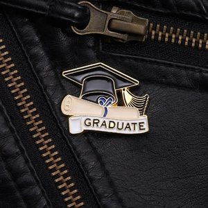 Macro shot of an enamel graduation cap brooch with GRADUATE banner on black leather