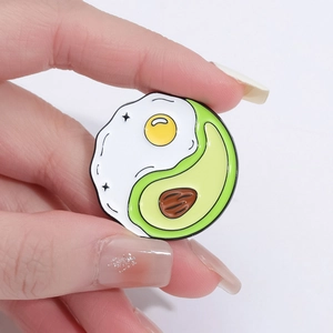 Close-up of creative round enamel pin featuring a fried egg and avocado yin-yang fusion design