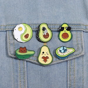 Detail of six creative avocado enamel pins showing cute cat and astronaut designs on denim