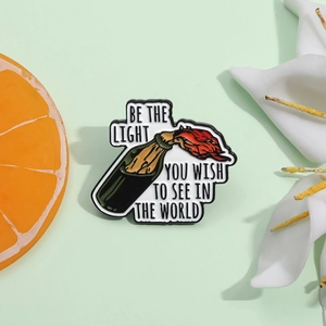 Emaille-Pin in Flaschenform mit Flamme und 'Be the light' Spruch auf grünem Grund
