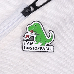 Dettaglio della spilla a dinosauro verde con testo 'I AM... UNSTOPPABLE' su tela