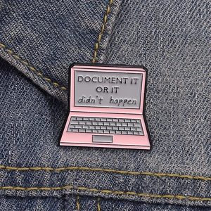 Pink laptop enamel pin with Document It Or It Didn't Happen quote on denim background