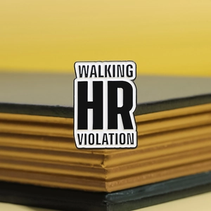 Detailed macro view of Walking HR Violation enamel pin on a book edge backdrop