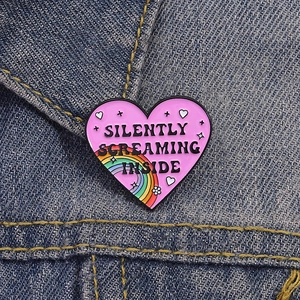 Close-up of heart enamel pin with Silently Screaming Inside text on denim fabric