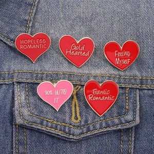 Five heart-shaped enamel pins with slogans on blue denim jacket pocket view