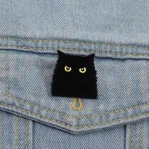 Gros plan d'un pin's chat noir en émail avec des yeux jaunes sur une veste en jean