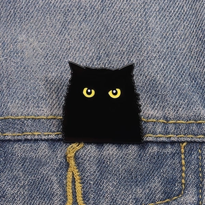 Détail d'un pin's chat noir mignon avec yeux jaunes fixé sur une poche de veste en jean