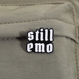 Dettaglio della spilla smaltata Still Emo appuntata su tessuto di tela verde