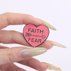 Pink heart enamel pin with FAITH over FEAR quote held in hand for size display
