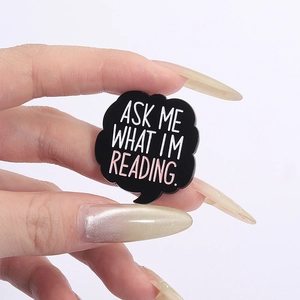 Black speech bubble enamel pin with ASK ME WHAT I'M READING quote for clothing