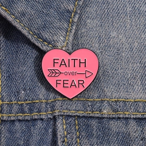 Pink heart enamel pin with FAITH over FEAR text shown on blue denim jacket