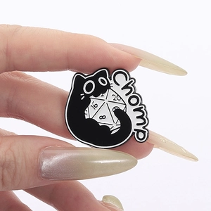 Cartoon black cat biting a D20 dice enamel pin badge with 'Chomp' text on white background