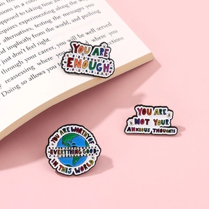 Close-up of three motivational enamel pins with colorful letters on a book page