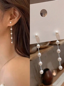 Close-up of long pearl drop earrings with five white pearls and silver metal chain
