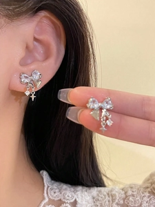 Détail de boucles d'oreilles nœud en zircon avec pompon argenté et pendentifs étoile