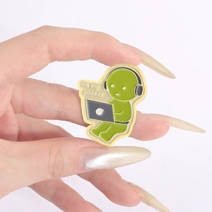 Macro shot of green cartoon enamel pin with headphones on my pooter text detail