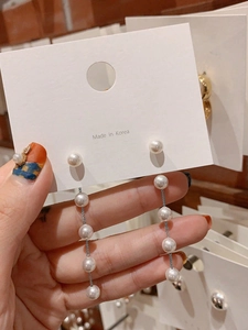 Detail of long drop pearl tassel earrings with five white pearls on a display card