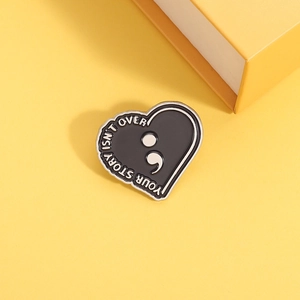 Detail of heart enamel pin showing Your Story Isn't Over text on a yellow background