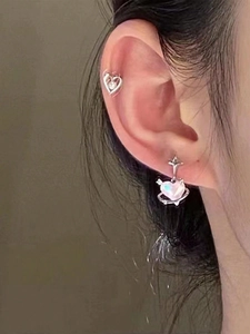 Detail of pink heart star stud earring and silver ear cuff on model with soft lighting