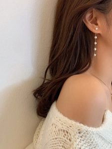 Elegant long pearl drop earrings with thin chain tassels shown on model with white knitwear