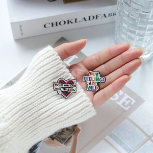 Creative enamel heart and letter lapel pins set held by hand over a white sweater