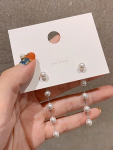 Detailed view of long hanging pearl chain earrings with vertical tassel design on card