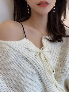 Detail view of pearl chain fringe earrings paired with white knit V-neck lace-up top