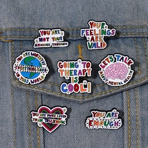 Set of 7 mental health enamel pins with motivational quotes on a denim jacket pocket