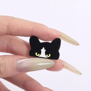 Close-up of a cute black cat enamel pin with yellow eyes held between fingers