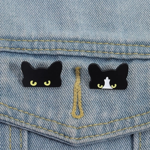 Macro shot of two cute cartoon black cat enamel pins pinned on blue denim jacket pocket