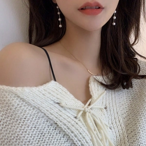 Fashionable long pearl earrings and gold smile necklace on a model wearing a white knit top