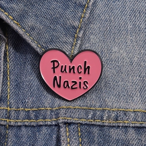 Pink heart enamel pin with Punch Nazis slogan on blue denim jacket pocket