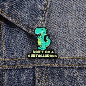 Funny green dinosaur enamel pin with a slogan on a blue denim jacket