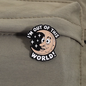 Detail of the 'I'M OUT OF THIS WORLD!' enamel pin on a green nylon backpack fabric