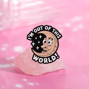 Macro shot of cartoon moon enamel pin with I'm out of this world text on pink crystal