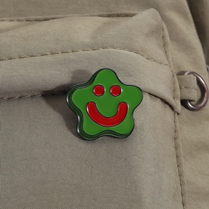 Close-up of a green star enamel pin with a red smiley face on khaki canvas fabric
