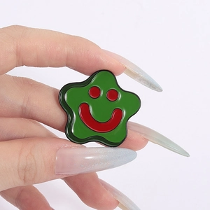 Green star-shaped enamel brooch with a red smiley face design held by hand