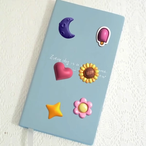 Close-up of 3D puffy cartoon stickers including heart and flower on a blue notebook