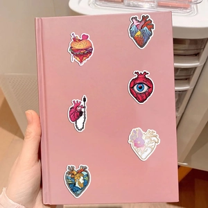 Nahaufnahme kreativer Herz-Aufkleber auf einem rosa Notizbuch mit anatomischen Designs