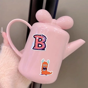Pink ceramic teapot with bow lid and colorful cartoon monster alphabet decals